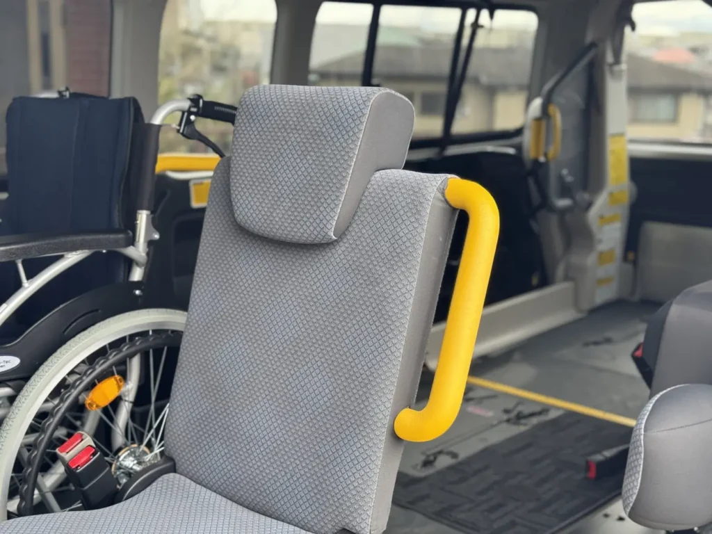 Attendant seat with yellow grab handles and wheelchair securement space