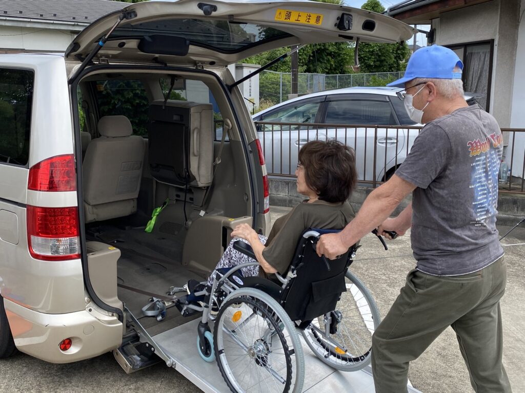 Driver assisting a passenger in a wheelchair up the rear ramp of our Toyota Noah in Yokohama